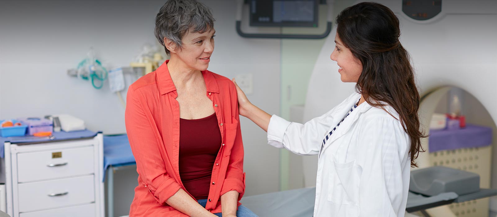 Mature female patient sitting on imaging machine consulted by radiologeist