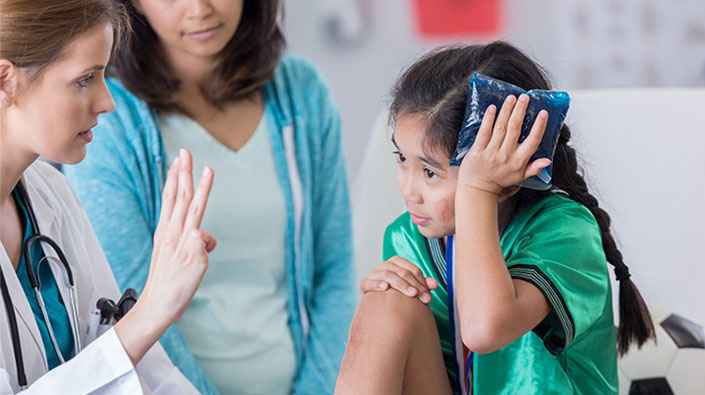 young athlete with hand on her head; doctor is holding up 3 fingers