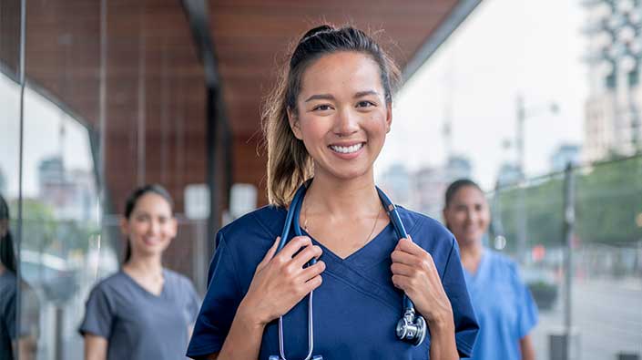 Three nurses smiling exterior of building