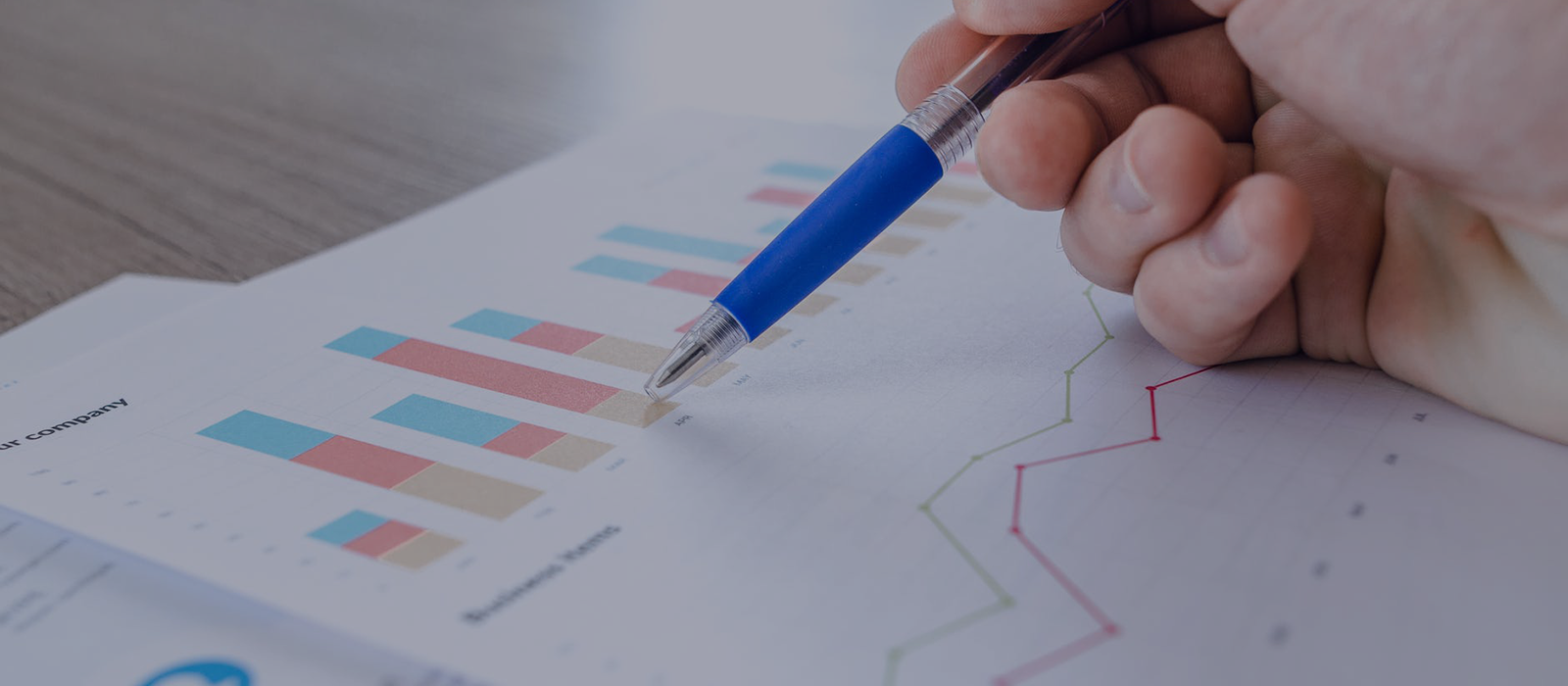 hand holding a pen over graphs on paper